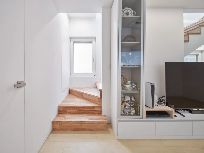 Landing: timber stair treads, glass display cabinet beside the TV unit, white walls, narrow window