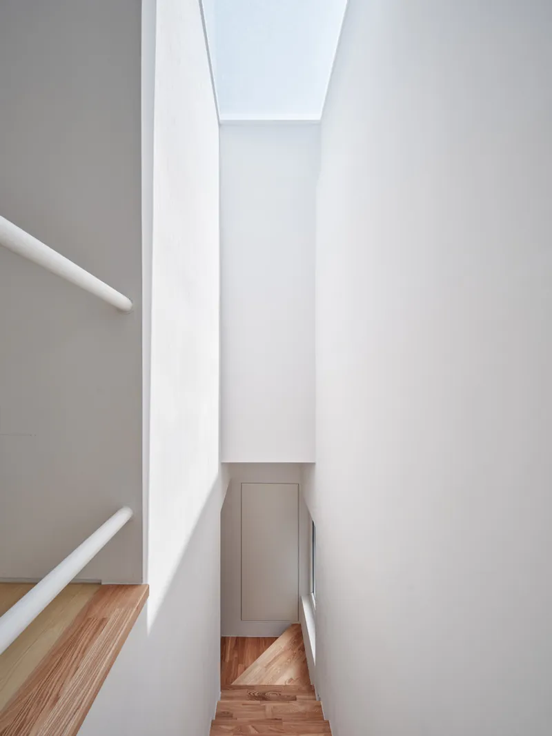 Stairwell looking up: narrow white walls tapering to a skylight at the top, daylight flooding down