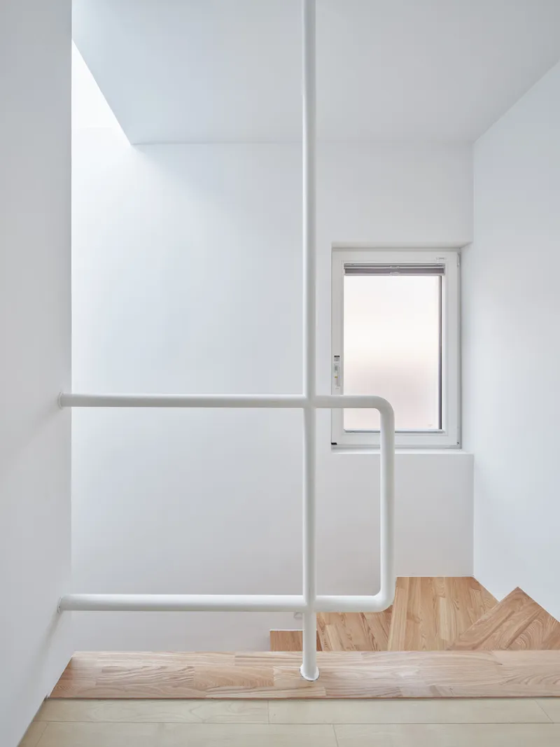 Stairwell from above: white metal railing, timber treads in herringbone, window, light washing the walls from above