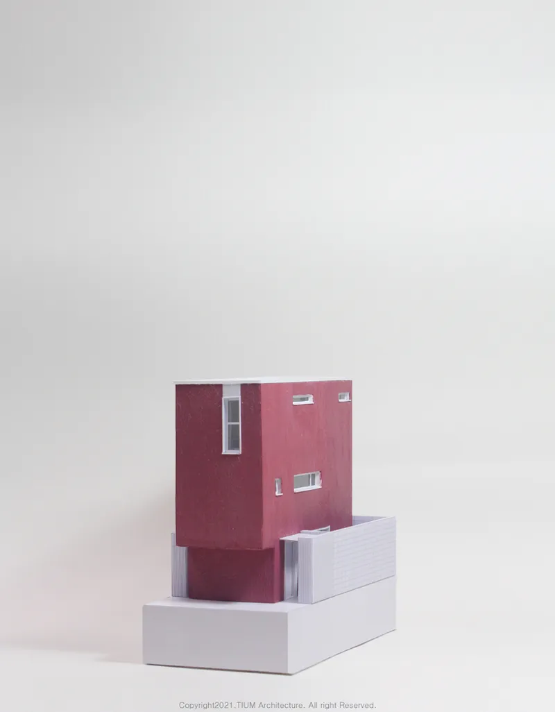 Physical model: pink upper volume sitting on grey and white base, showing the angular massing