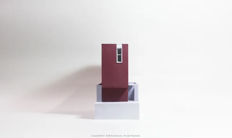 Physical model front: pink tower on white base, narrow vertical window, clean geometric form