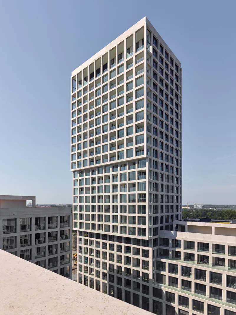 Grid facade of white concrete frames and recessed dark balconies rising against a clear blue sky