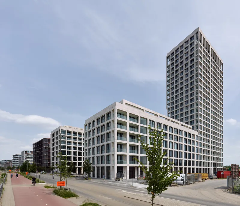 Street view of tiered residential blocks with white concrete frames and glazed balconies under a pale sky