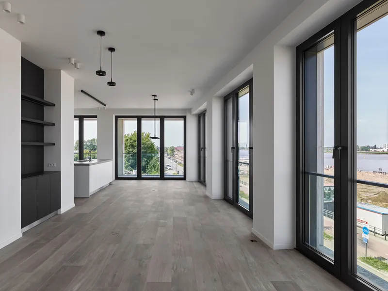 Open living space with dark timber floors, white kitchen peninsula and floor-to-ceiling windows overlooking the waterfront