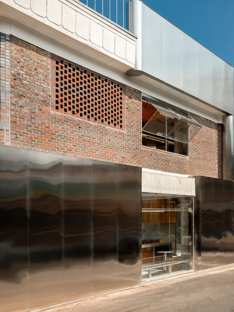 Street facade with perforated brick screen above corrugated metal panels under clear blue sky