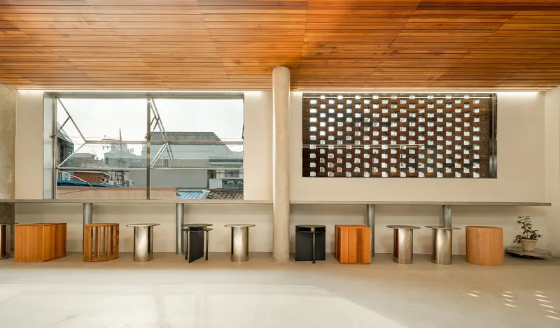 Perforated brick window and large glazed opening above built-in seating with cylindrical stools