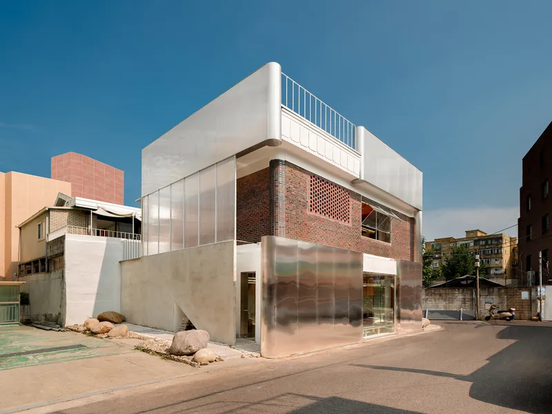 Corner view of the stacked volumes with translucent panels and perforated brick at dusk