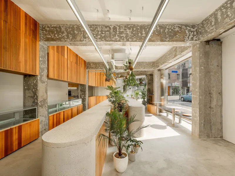 Interior with exposed concrete beams, timber cabinetry, and potted palms in white planters
