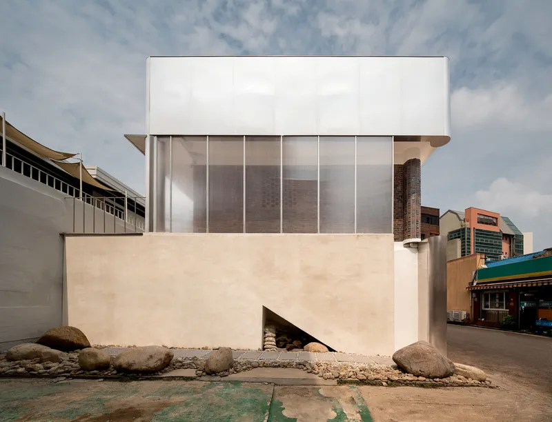Street facade showing white stucco base with triangular entrance beside boulders and gravel