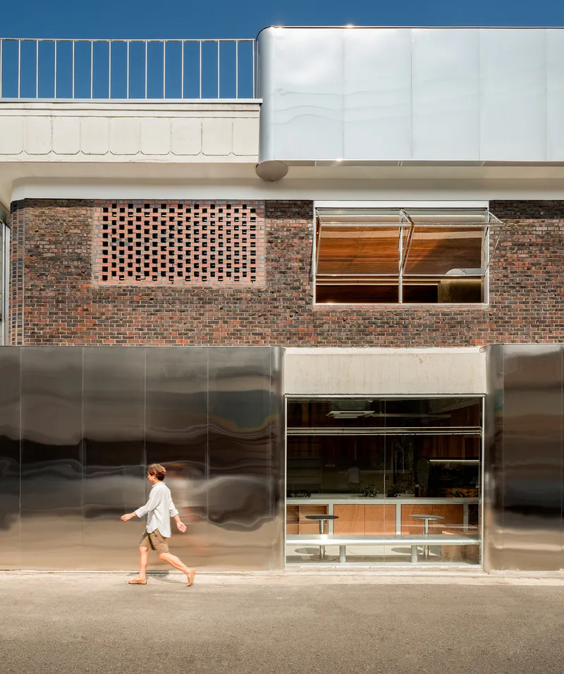Reflective steel facade with person walking past the perforated brick above