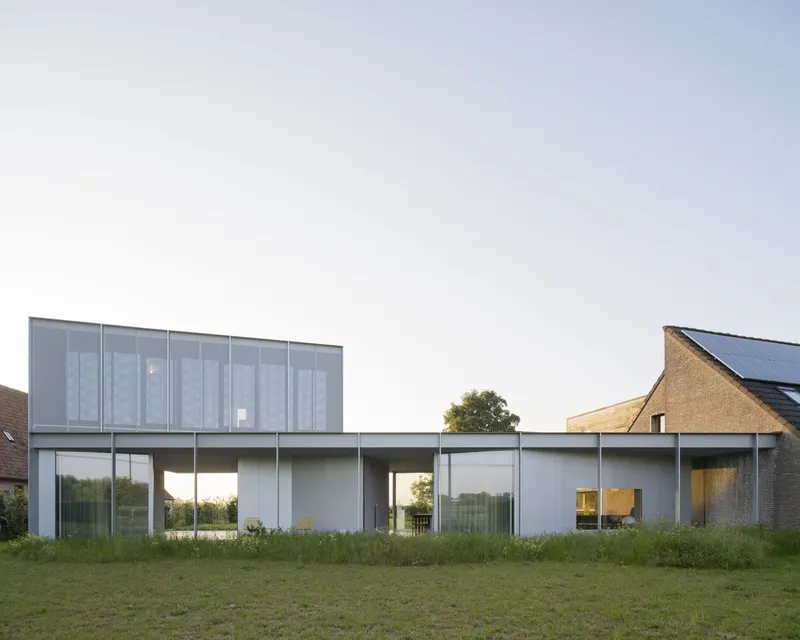 Garden facade showing horizontal white volume with floor-to-ceiling glass and translucent upper story in long grass