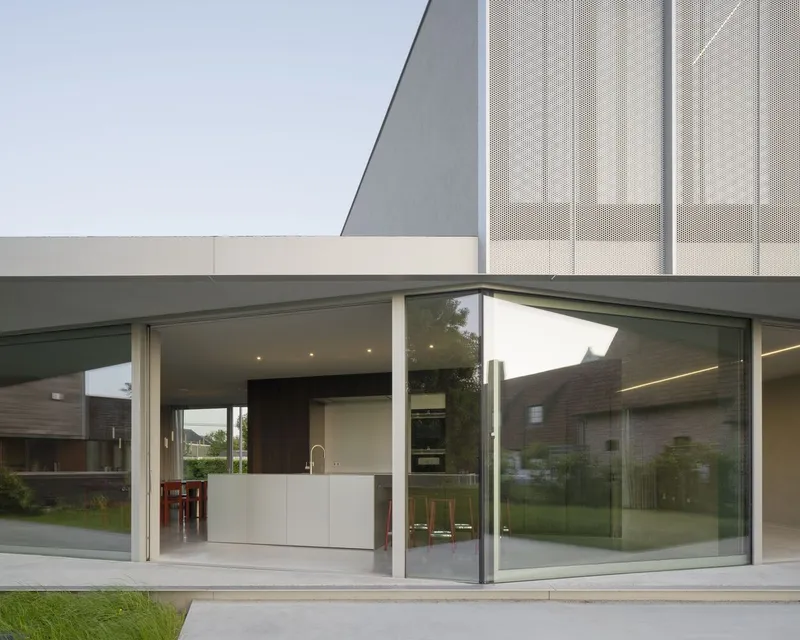 Open sliding glass corner framing kitchen island beneath cantilevered upper volume with perforated metal cladding