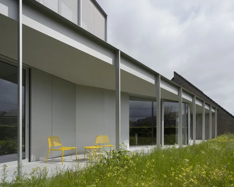 Covered terrace with yellow chairs and full-height glazing bordered by tall wildflower meadow
