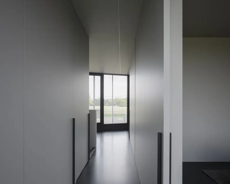 Corridor view through floor-to-ceiling white panels leading to a framed landscape window