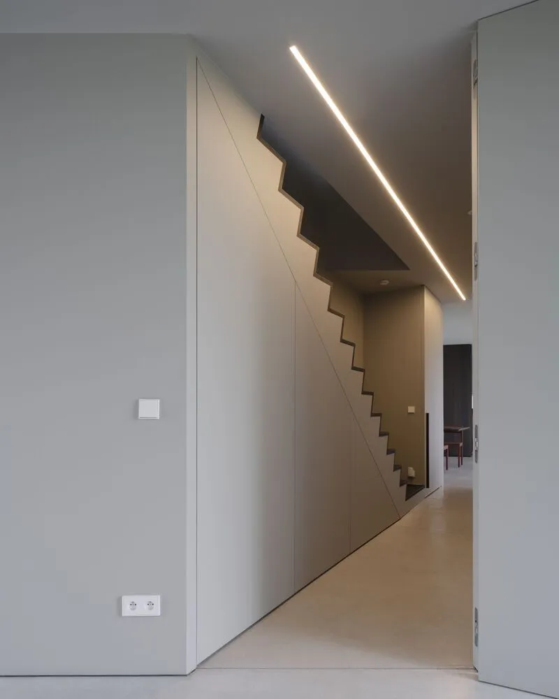 Interior hallway with concealed staircase behind angled white paneling and recessed linear ceiling light