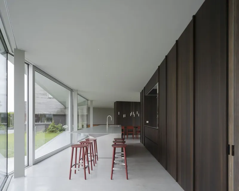 Kitchen counter with terracotta bar stools and vertical timber-panelled wall alongside continuous glazing