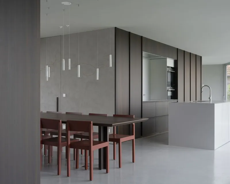 Dining table with terracotta chairs beneath tubular pendant lights and concrete accent wall
