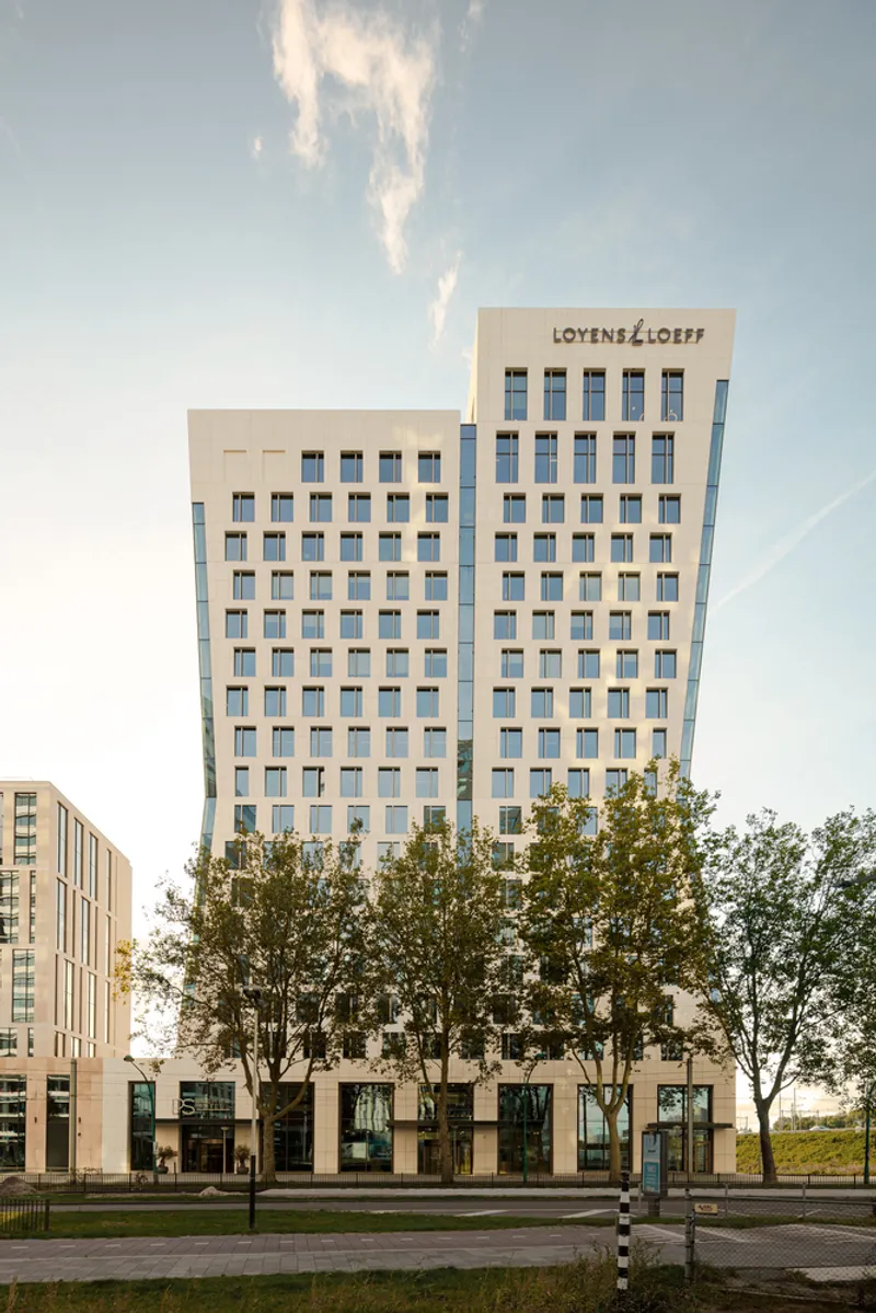 Frontal view of the twin tower facades with repetitive window pattern and street trees at base