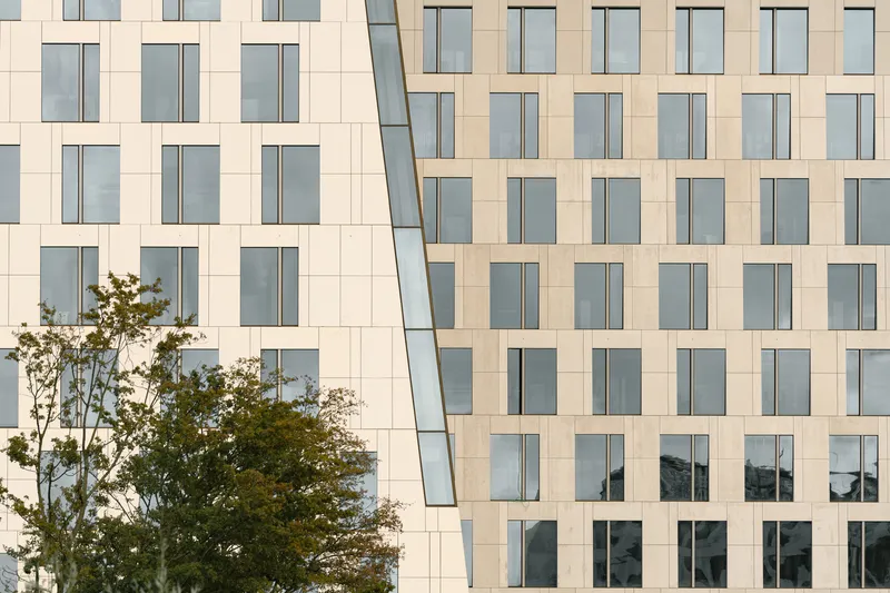 Close-up of the facade showing angled glazed slot and regular grid of windows with a tree