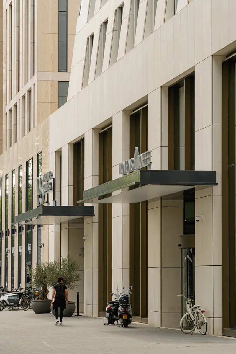 Ground-level view of the entrance canopies and light-colored panel cladding with pedestrians and bicycles
