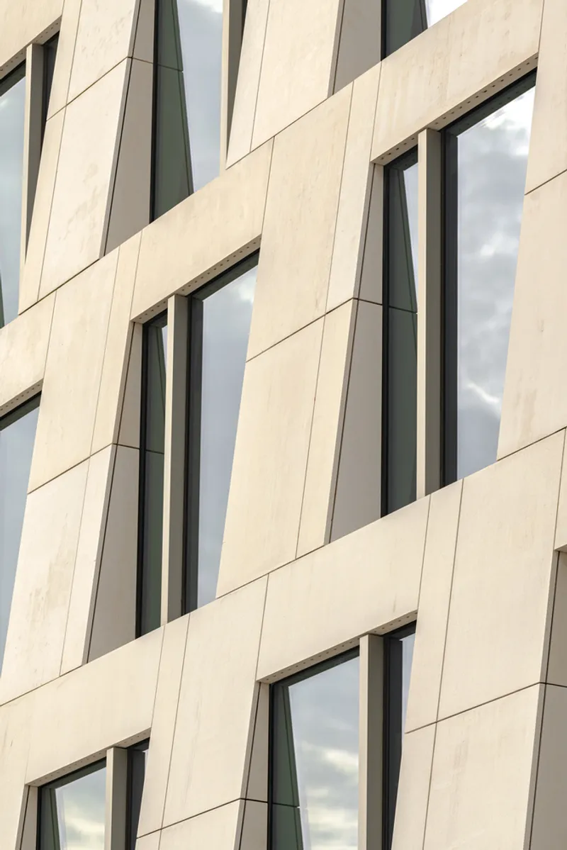 Facade detail showing angled limestone panels with vertical window openings under cloudy skies