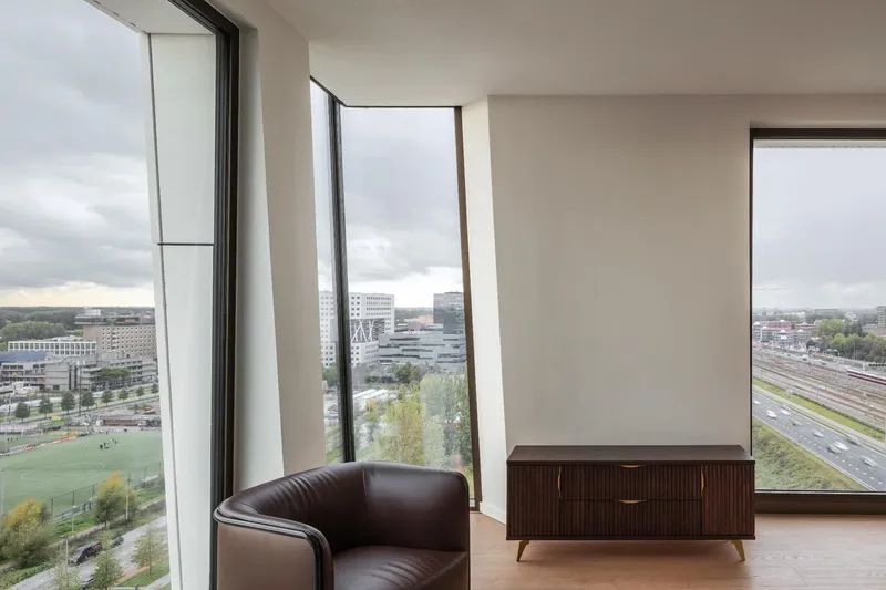 Interior corner with canted floor-to-ceiling windows overlooking railway tracks and autumn trees