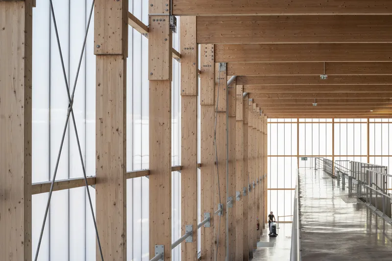 Interior balcony with timber posts and cross-bracing overlooking the main circulation corridor with a lone figure