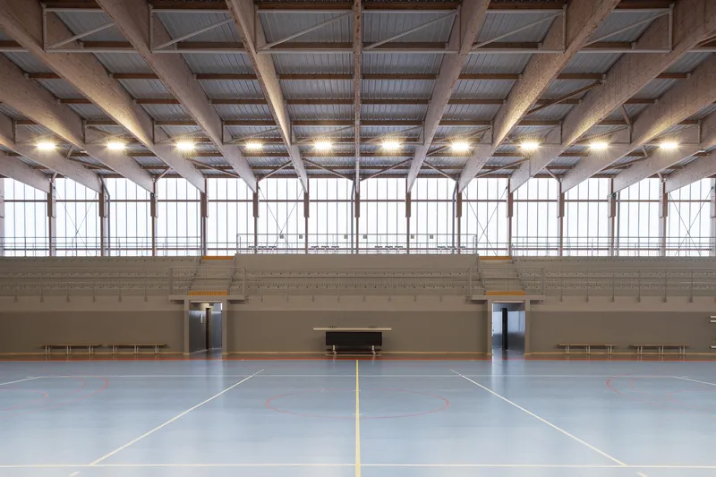 Sports hall with exposed timber beam ceiling, arched clerestory windows and painted lines on the blue floor