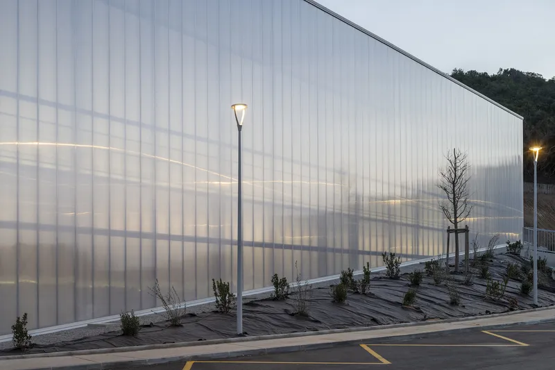 Translucent exterior wall at dusk with interior lights casting shadows of structural framing through the polycarbonate panels