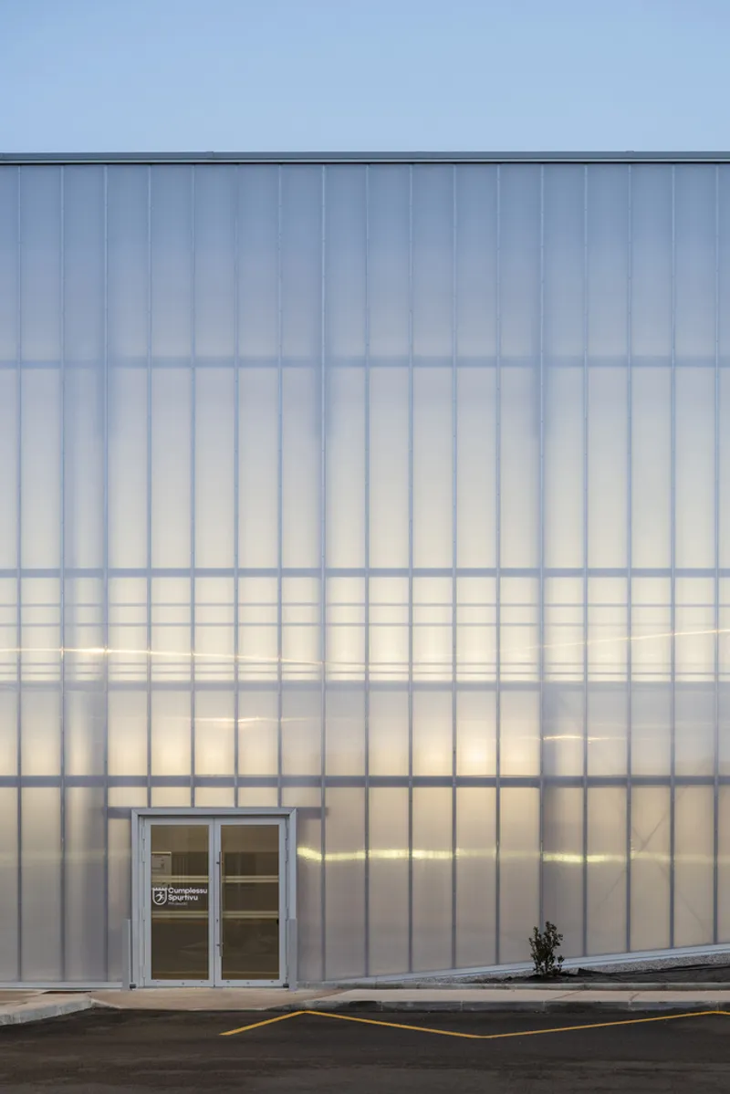 Translucent corrugated polycarbonate facade with vertical ribbing and a white double door at ground level