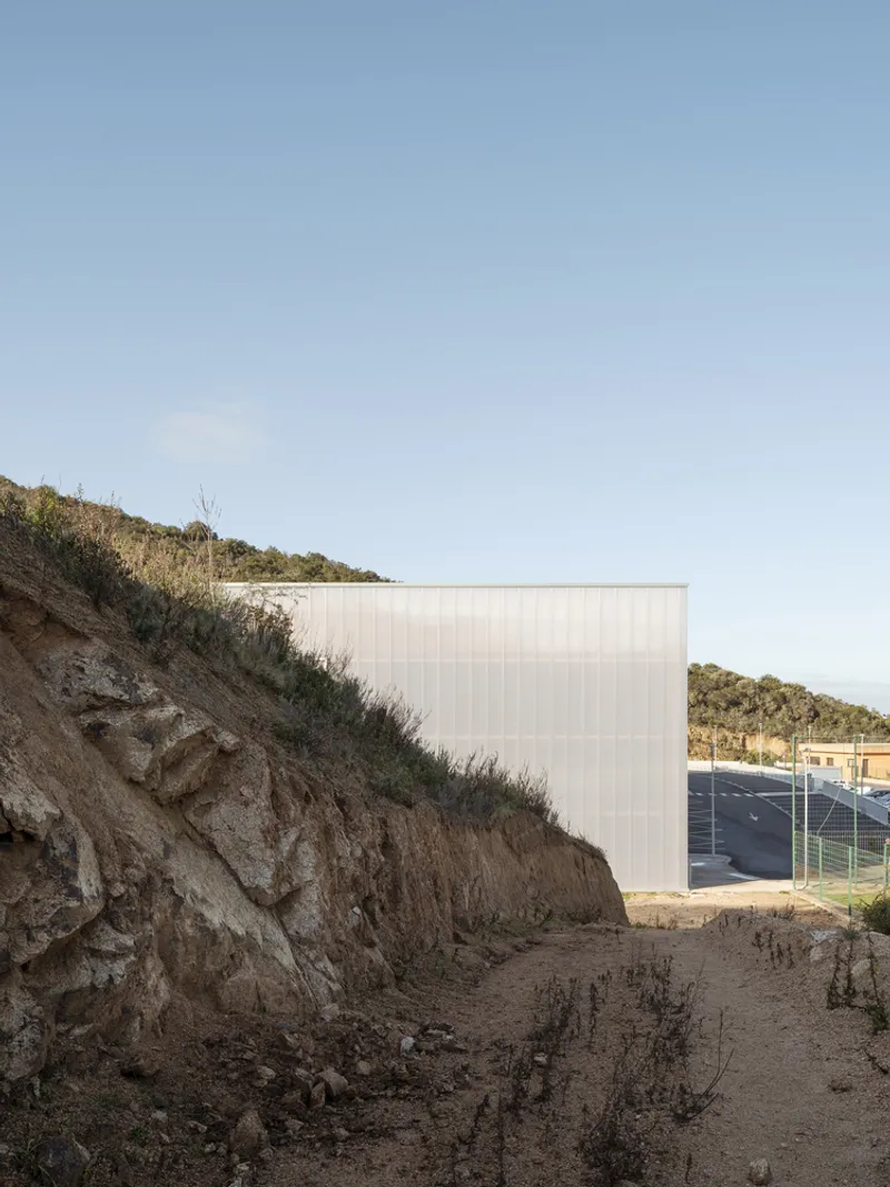 Ribbed metal wall rising from an excavated hillside with exposed rock and sparse vegetation