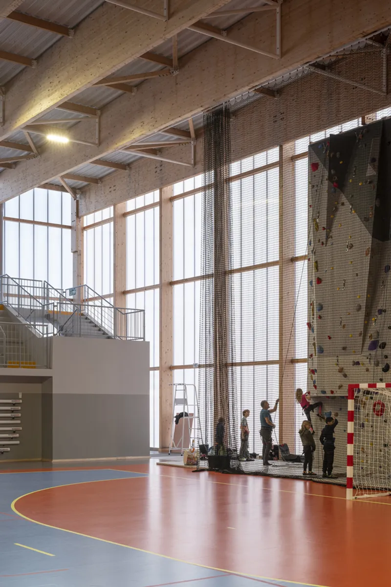 Tall glazed wall with metal mesh divider and people gathered near a climbing wall