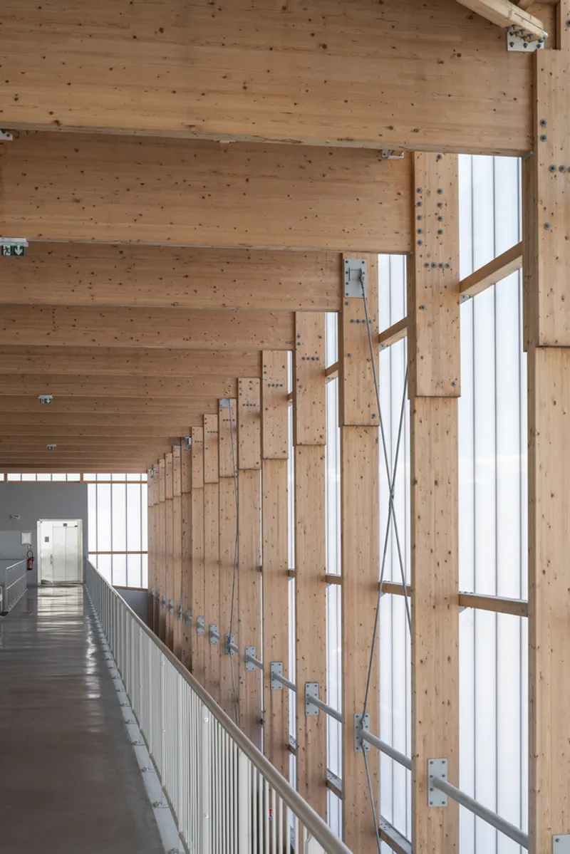 Interior corridor with laminated timber columns and beams beside a floor-to-ceiling glazed wall