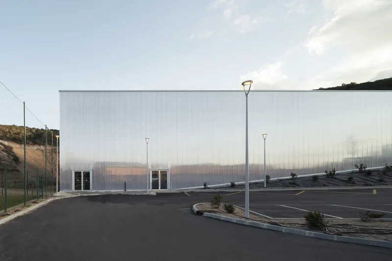 Corrugated polycarbonate wall stretching across an empty parking lot under a cloudy sky