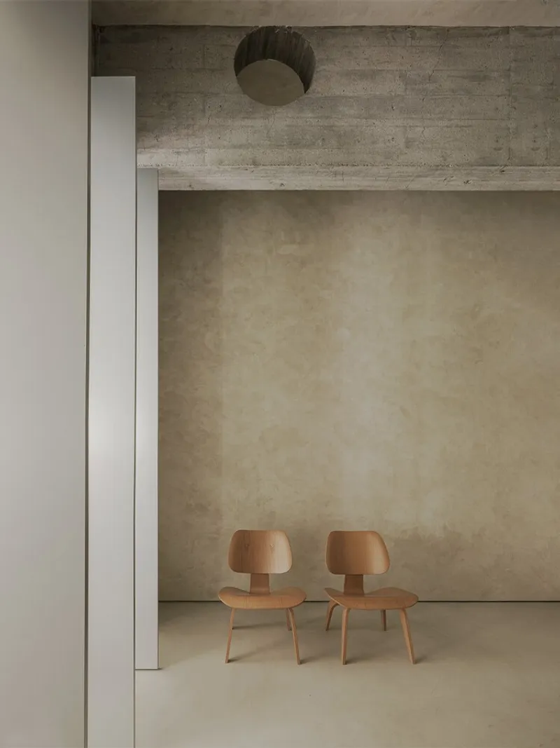 Two bentwood chairs beneath a board-formed concrete beam and recessed ceiling dome in a pale alcove