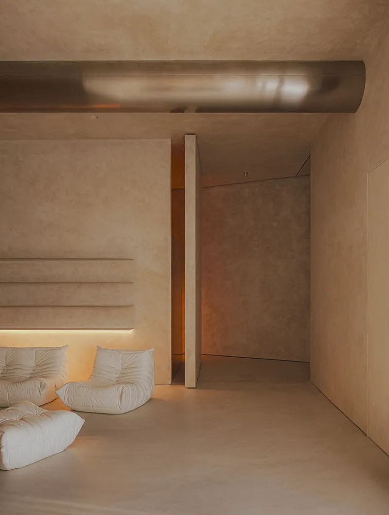 Living area with white upholstered sofa beneath an exposed cylindrical duct and textured plaster walls