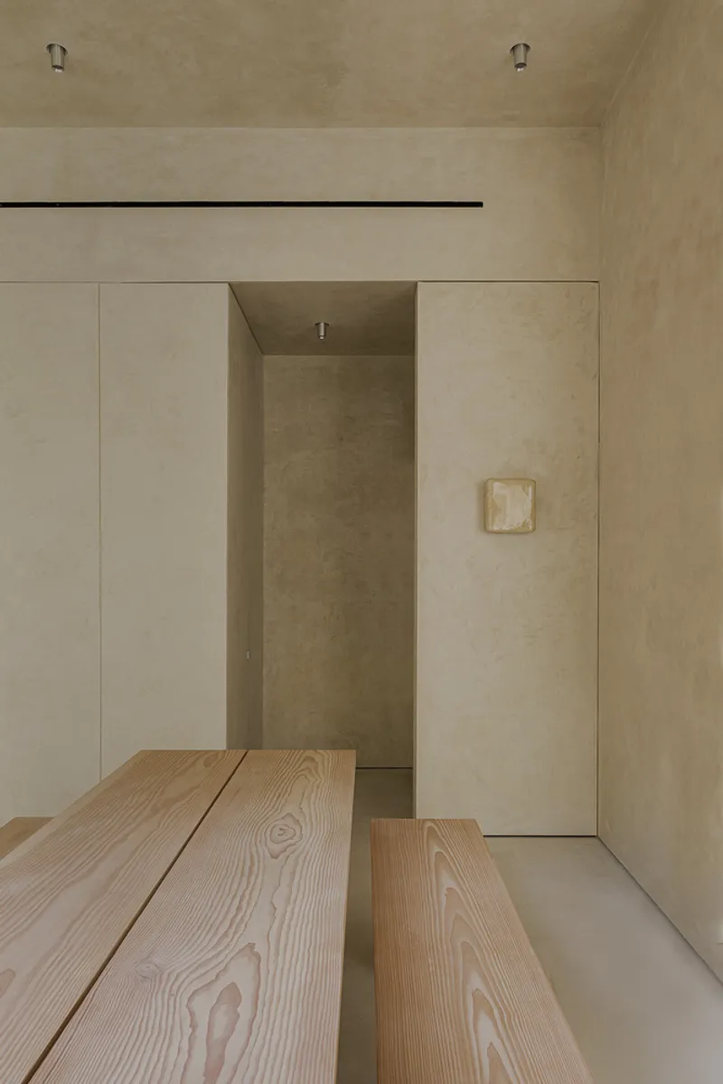 Timber dining bench extending toward a recessed alcove with flush wall panels and a small relief artwork