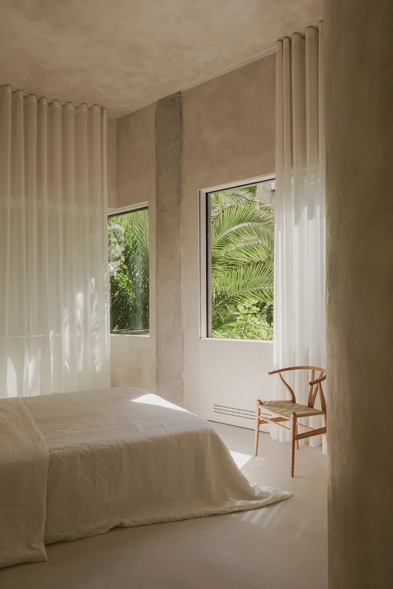 Bedroom with twin windows framing palm fronds and dappled sunlight on sheer curtains