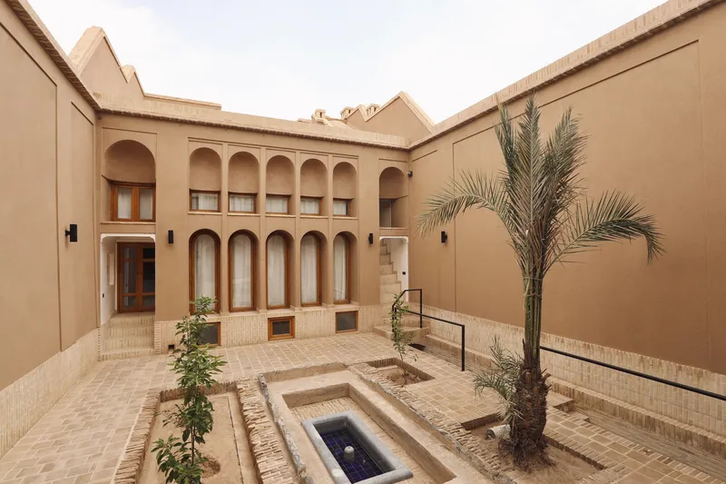 Corner view of the courtyard showing arched arcades, central water feature and planted palms