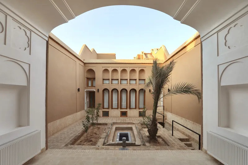 View through arched opening to courtyard with sunken fountain and palm at golden hour