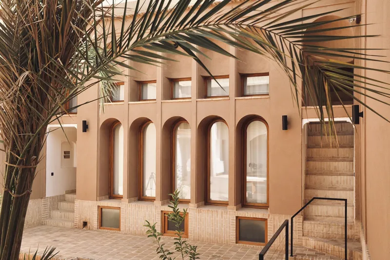 Courtyard facade with arched windows and brick detailing framed by palm fronds