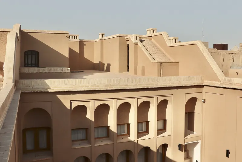 Rooftop view of the two-story courtyard with arched openings and rendered walls in afternoon light