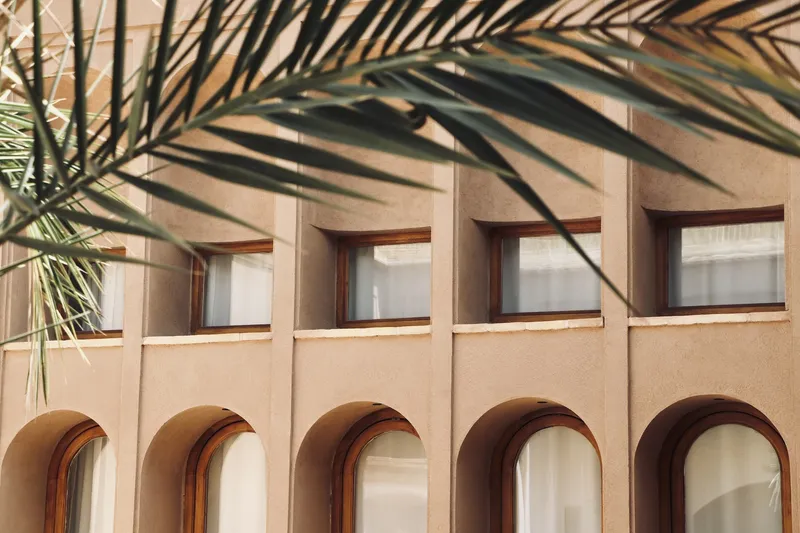Facade detail showing rectangular and arched windows with palm shadows cast across the surface