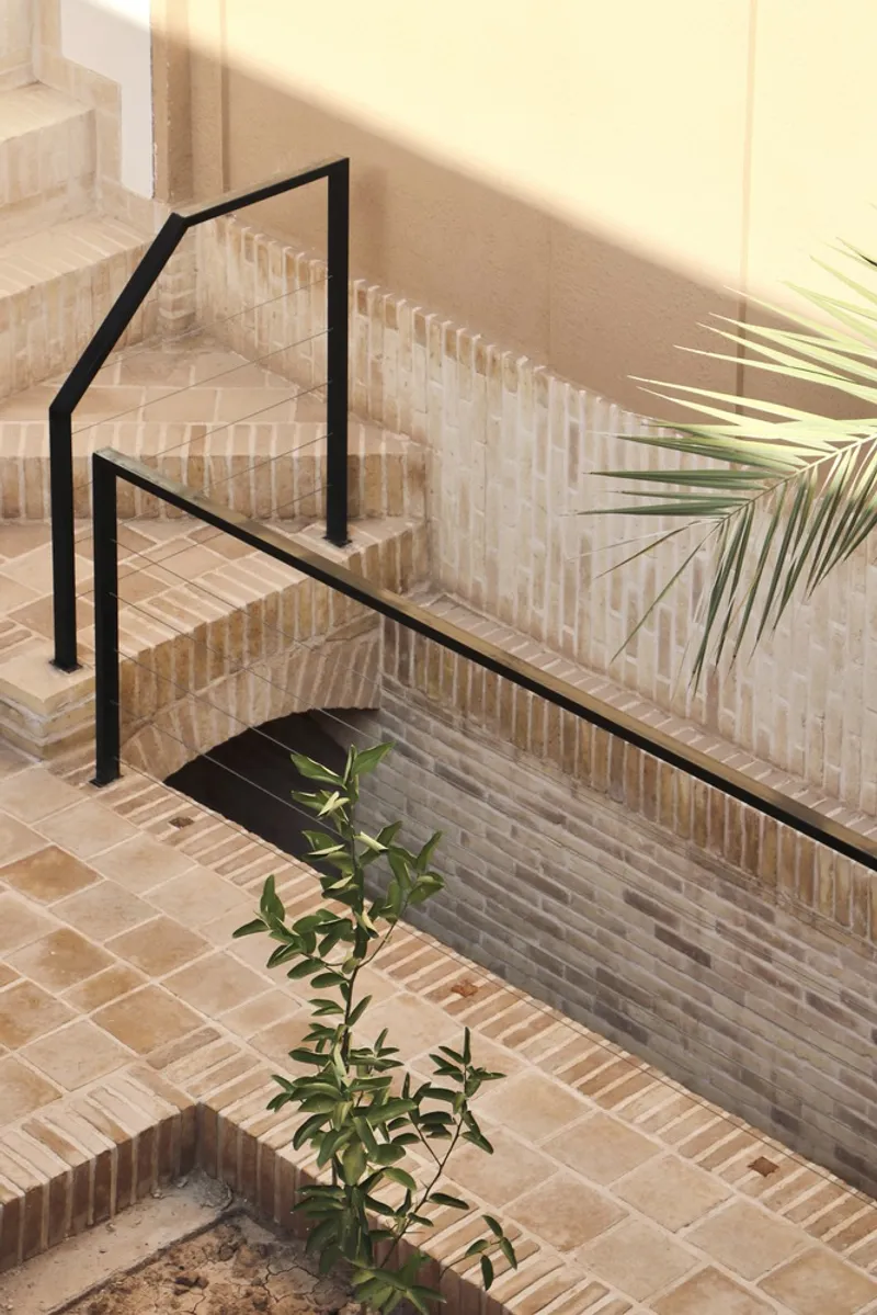 Brick staircase with black steel handrail and palm fronds casting shadows in warm sunlight