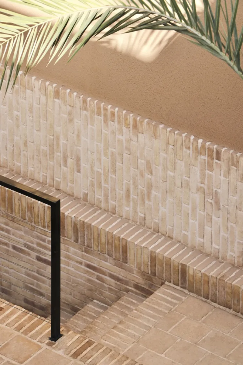 Close-up of woven brick balustrade with steel railing and palm shadow on plastered wall above
