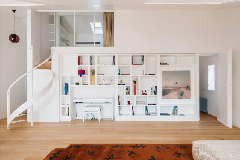 White shelving unit with integrated piano niche and spiral staircase in light-filled living room