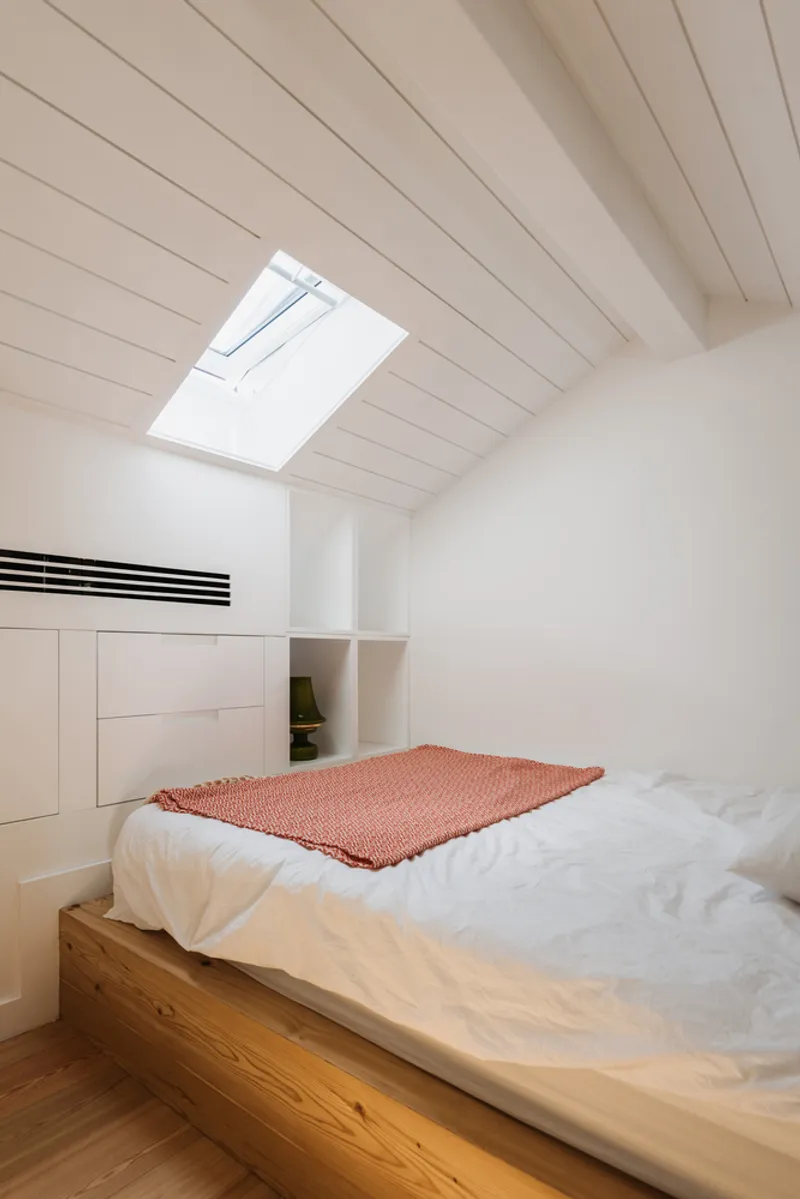 Bedroom with oak platform bed under a sloped wood plank ceiling and skylight