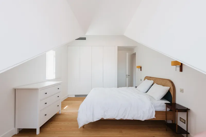 Attic bedroom with white built-in wardrobes under a pitched ceiling with two small windows