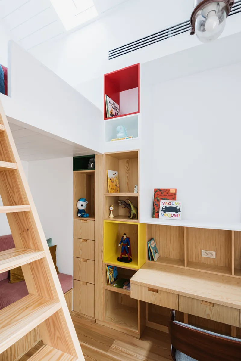 Light wood storage wall with red and yellow cubbies beneath a double-height ceiling with skylight