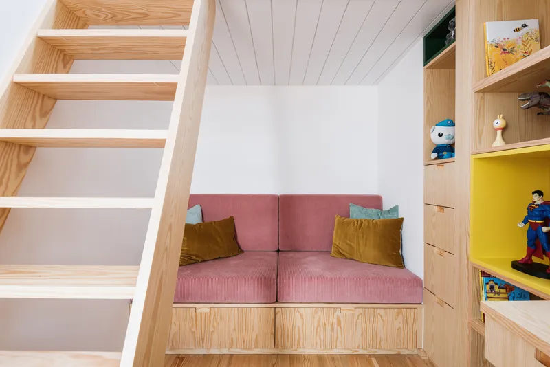 Built-in plywood bench with pink upholstered cushions flanked by storage shelving under wood slat ceiling